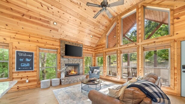 A cabin interior with a stone fireplace, a television, a couch, and large windows.