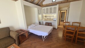 Une chambre à coucher comprenant un lit, une table en bois, une chaise, un petit coin cuisine et une salle de bain visible à travers une porte ouverte.