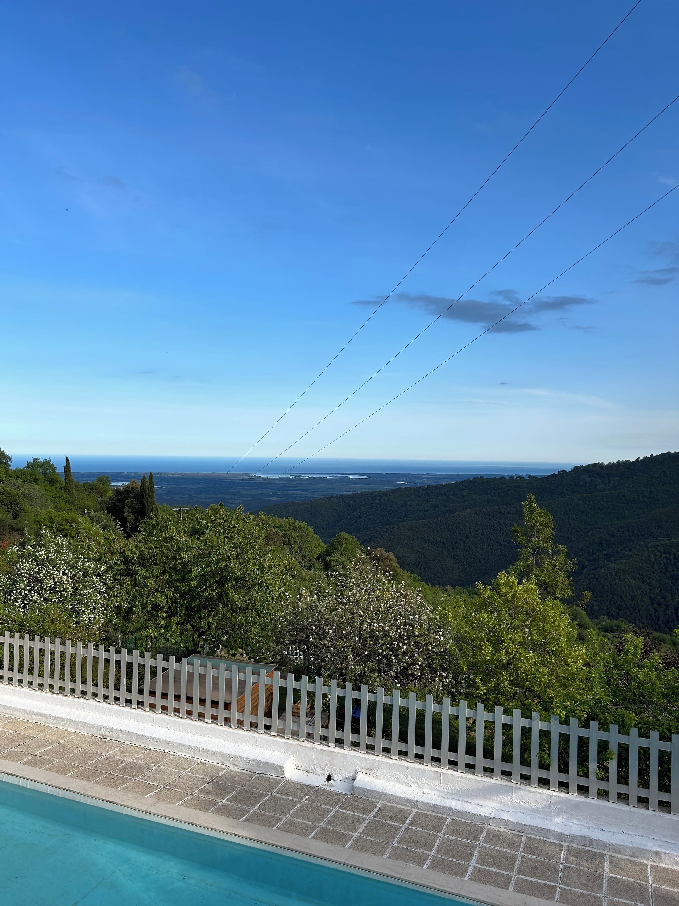 A swimming pool with a white fence, surrounded by lush greenery and a view of a distant landscape.