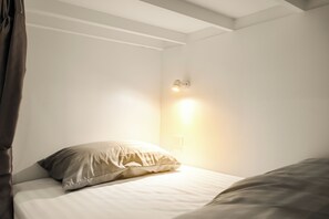 A neatly made bed with a pillow and a bedside lamp in a room with white walls and a sloped ceiling.