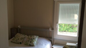 Ein Schlafzimmer mit einem Bett, einem Nachttisch, einem Fenster mit Jalousien und einer Deckenleuchte.