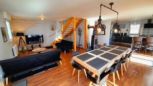 A modern living space with a large dining table, a sofa, and a staircase leading to an upper level.