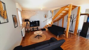 A living room with a wooden floor, a black sofa, a TV, and a staircase.