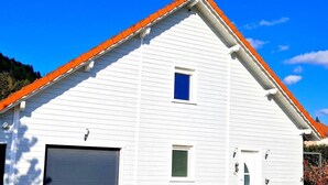 A white two-story building with a red roof, a garage, and a small window.