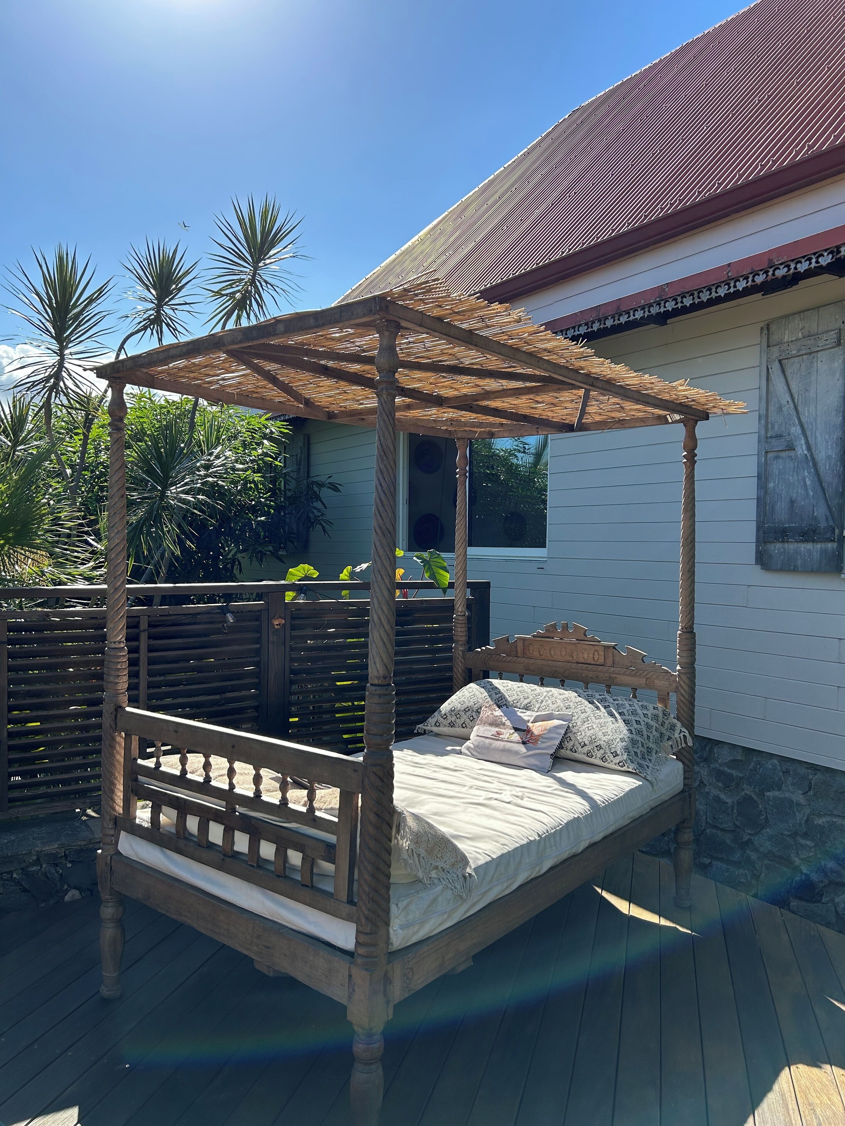 Un lit à baldaquin en bois, posé sur une terrasse en bois.