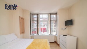 A bedroom with a bed, a window with curtains, a television on a dresser, and a radiator under the window. - Kunda House Dawlish (Birmingham)