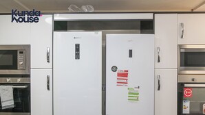 A kitchen with a built-in microwave, a built-in oven, and two white refrigerators with various stickers and labels. - Kunda House Dawlish (Birmingham)