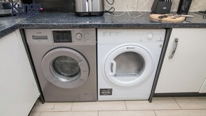A compact kitchen with a washing machine and a coffee maker. - Kunda House Dawlish (Birmingham)