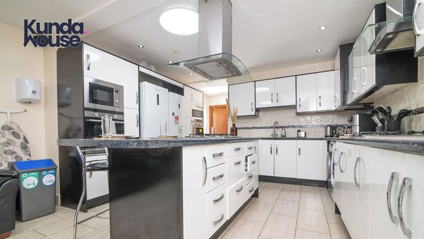 A modern kitchen with white cabinets, a black countertop, stainless steel appliances, and a glass backsplash. - Kunda House Dawlish (Birmingham)