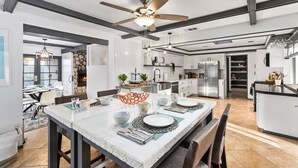 A modern kitchen with white cabinetry, a central island, and a dining area with a white table and chairs. - 30% Off September, Great 4 Families -Pool, Jacuzzi (Palm Springs)