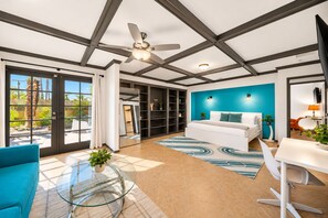 A modern bedroom with a bed, a desk, and a chair. There is a large window and a ceiling fan.