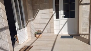 Un espace extérieur abrité, doté de murs en pierre, de deux portes blanches et d’un pot de fleurs suspendu.