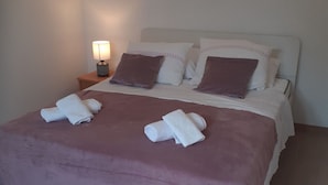 Un lit bien fait, recouvert d’une couvre-lit violette, avec deux serviettes blanches et une lampe de chevet.