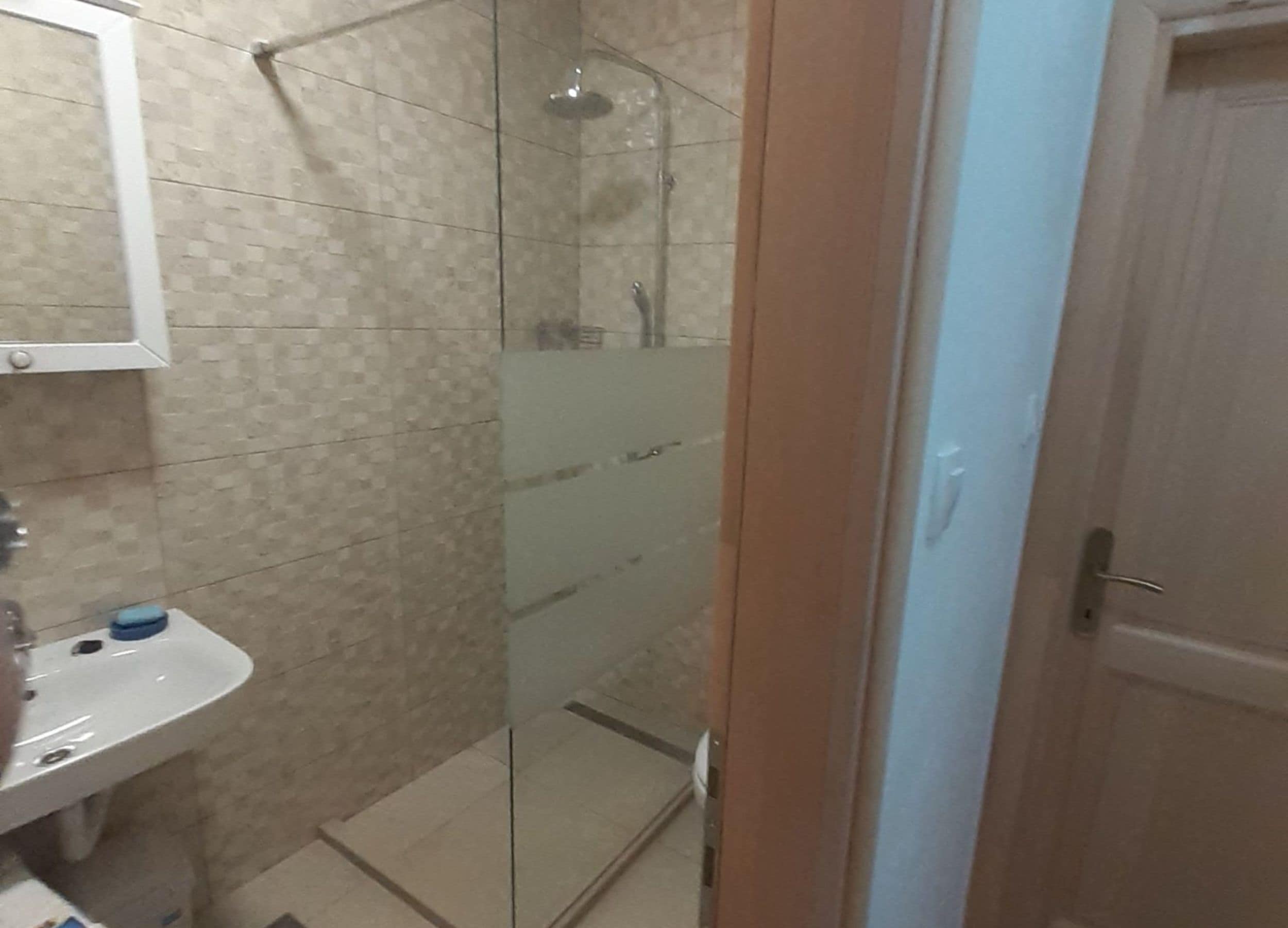 Ein Badezimmer mit Duschkabine aus Glas, einem weißen Waschbecken und einem Spiegel darüber.