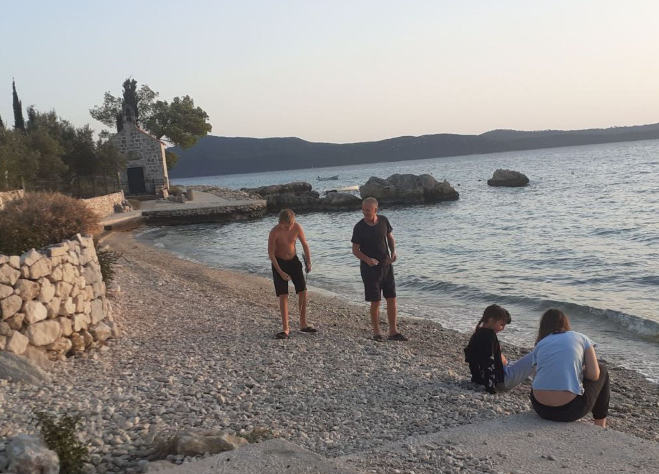 A pebbled beach with a stone wall and a small building.