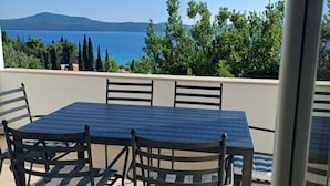 Une terrasse avec une table et des chaises, une vue sur la mer et une montagne à l’horizon.