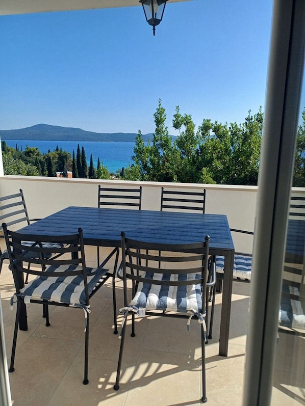 A terrace with a table and chairs, a view of the sea, and a mountain in the distance.