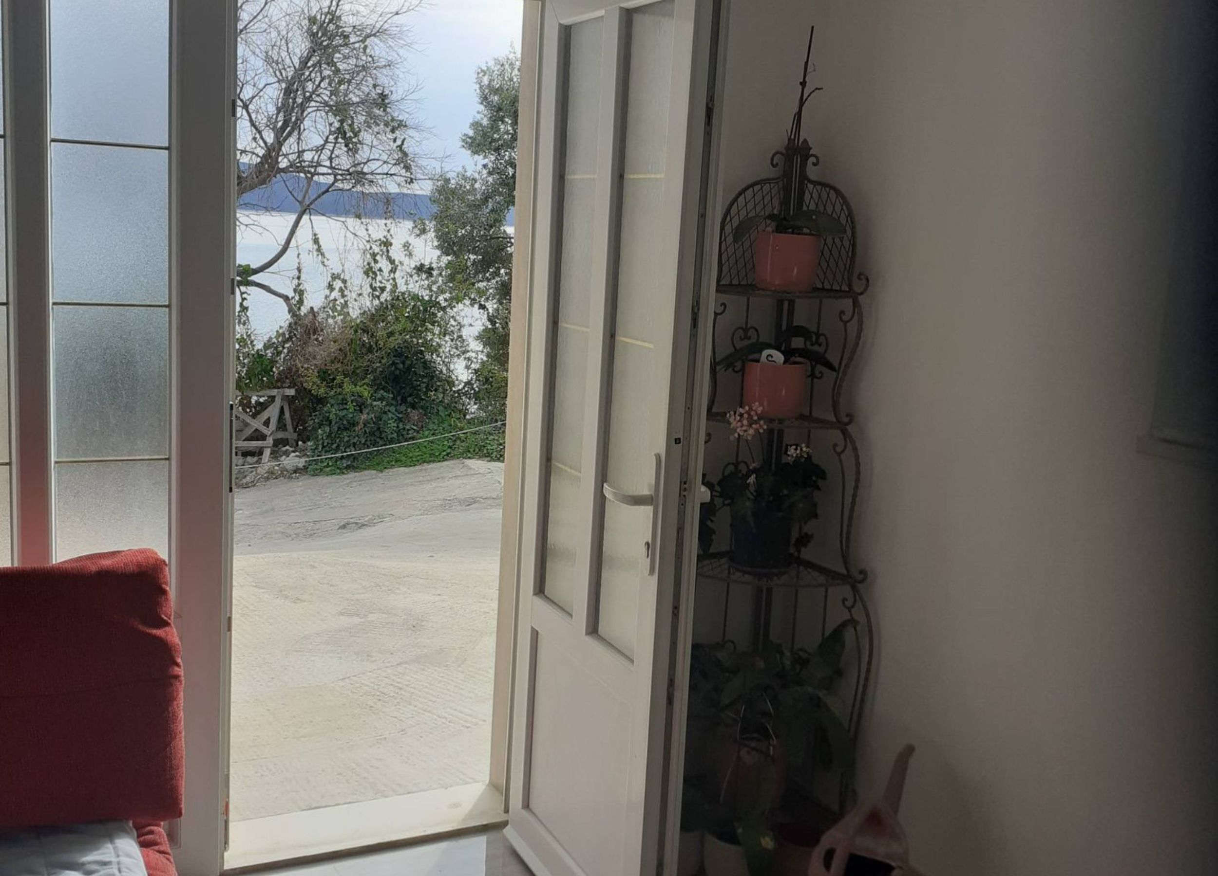 Una stanza con una grande finestra, una sedia rossa e un espositore metallico con diverse piante in vaso.