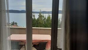 Un balcon avec une table et des chaises à carreaux, donnant sur une étendue d’eau et sur des collines lointaines.