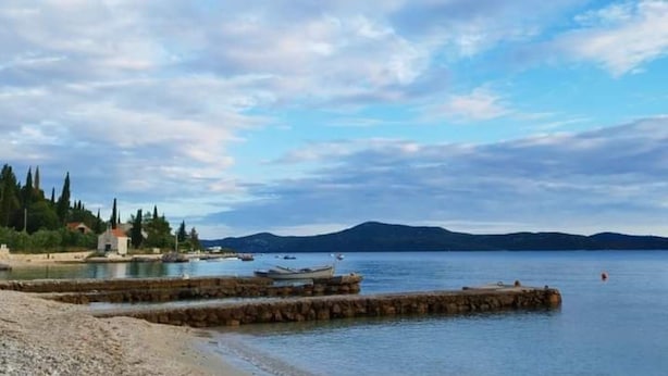 Un paysage côtier avec une rive rocheuse, un petit bâtiment et des bateaux sur une eau calme.