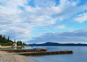 A coastal scene with a rocky shoreline, a small building, and boats on calm water.