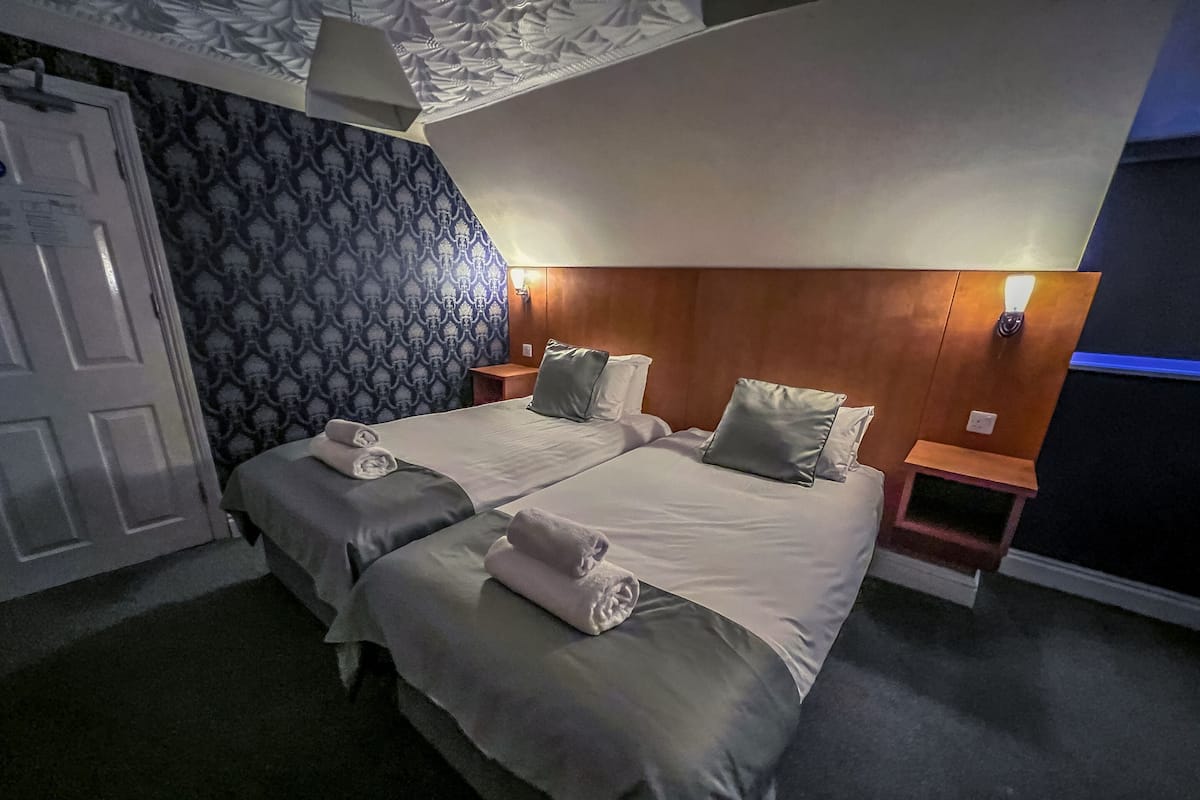 A double bed with two pillows, a bedside table, and a wall-mounted lamp.