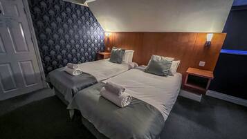 A double bed with two pillows, a bedside table, and a wall-mounted lamp.