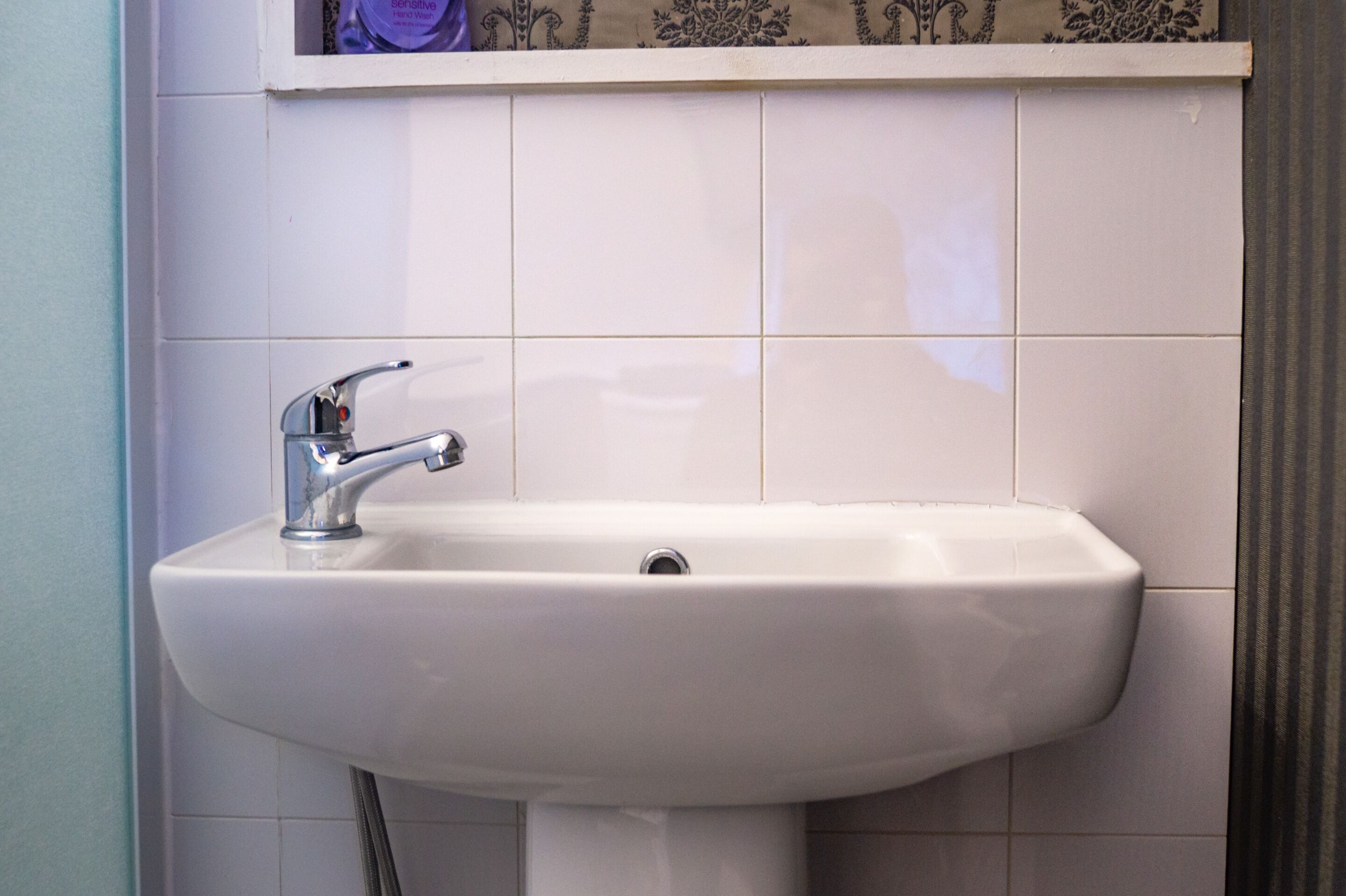 A white bathroom sink with a chrome faucet, set against a tiled wall.