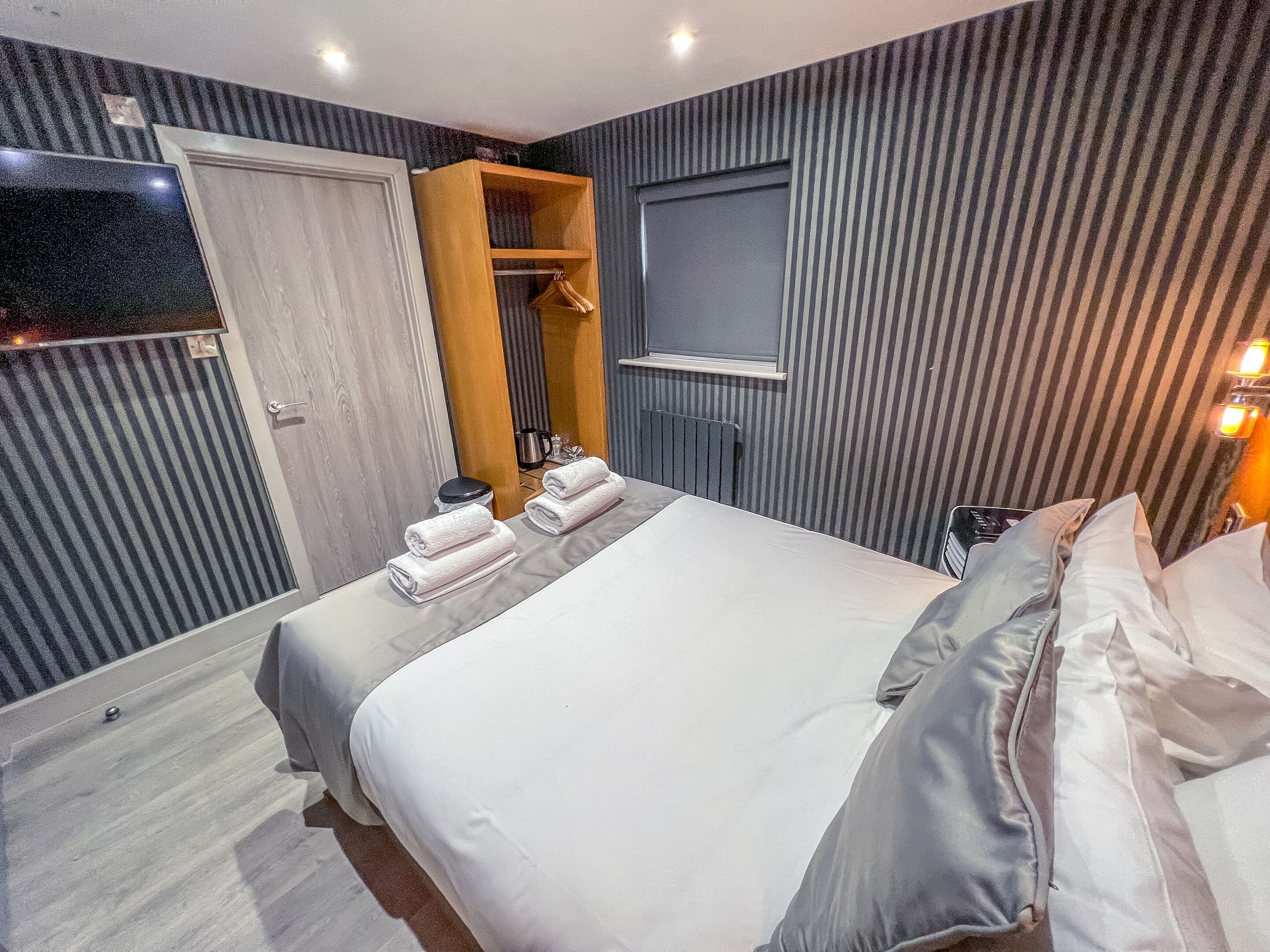 A hotel room with two beds, a wooden wardrobe, a mirror, and a TV.