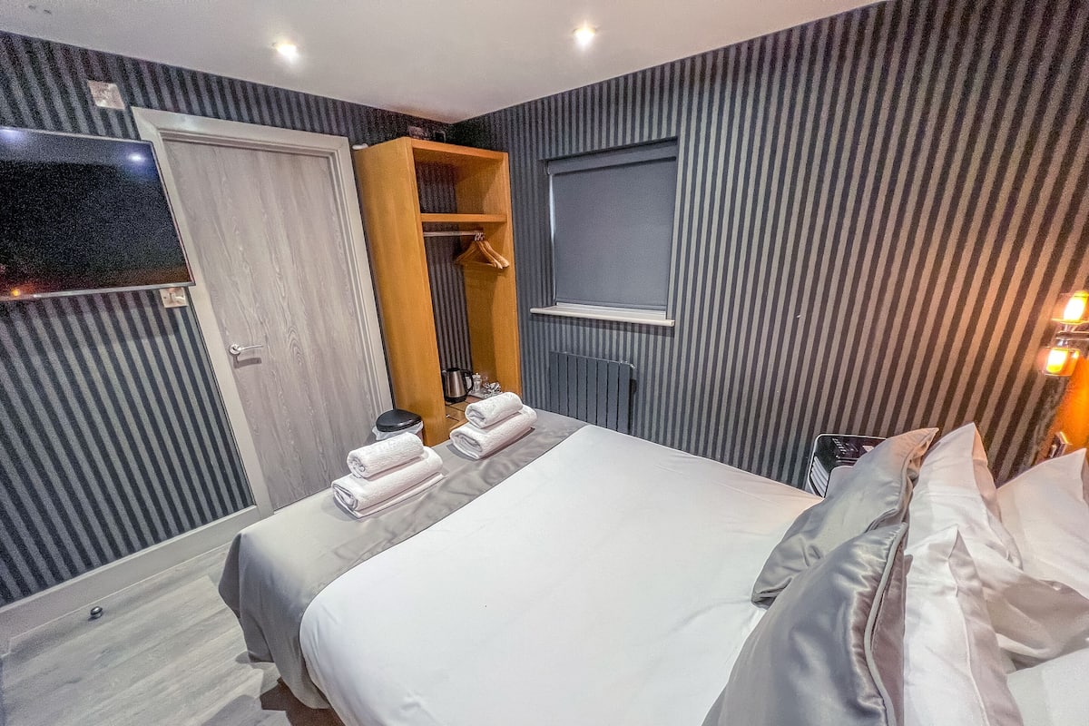 A hotel room with two beds, a wooden wardrobe, a mirror, and a TV.
