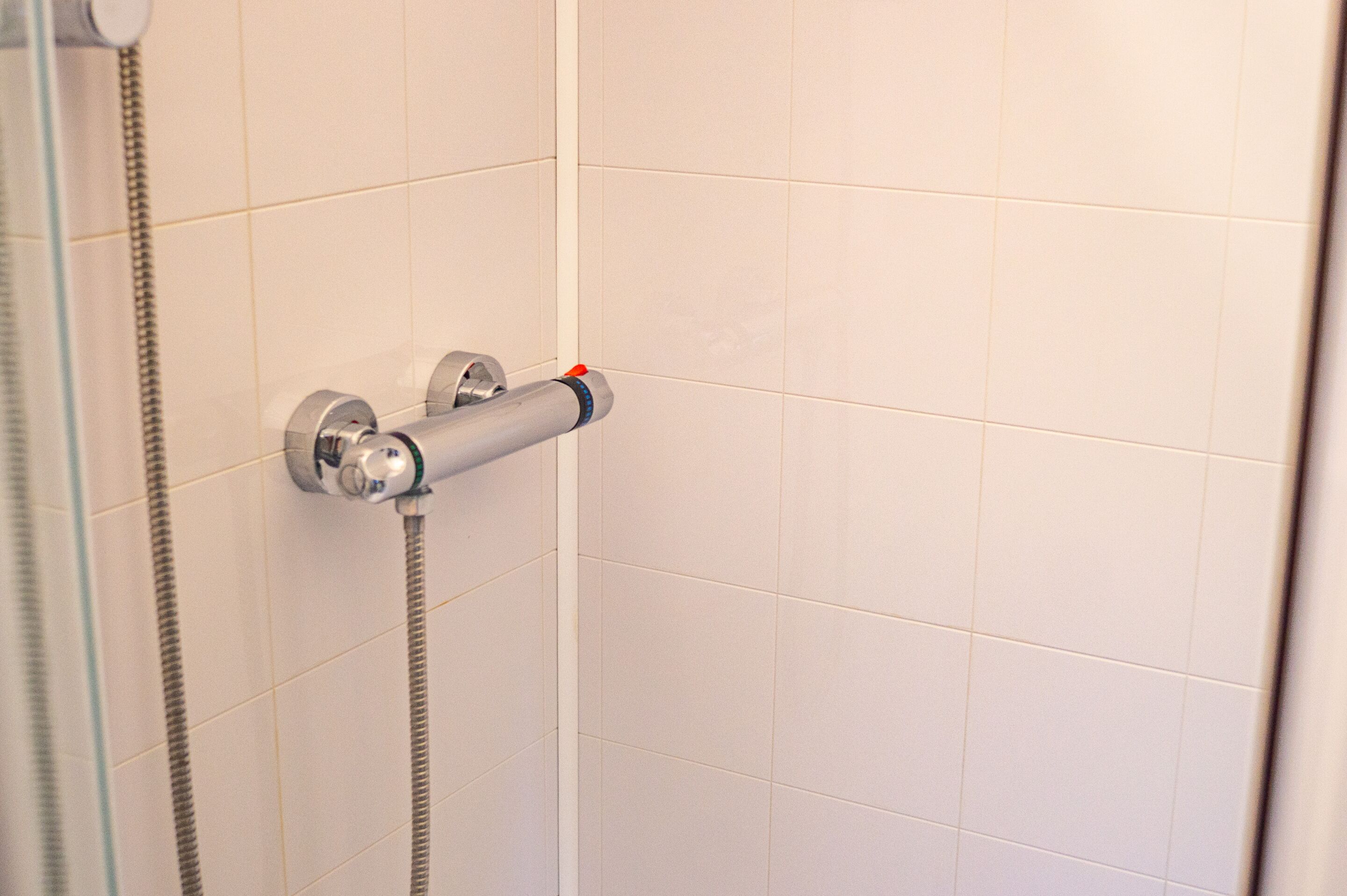 A shower with a handheld showerhead and a wall-mounted control valve.