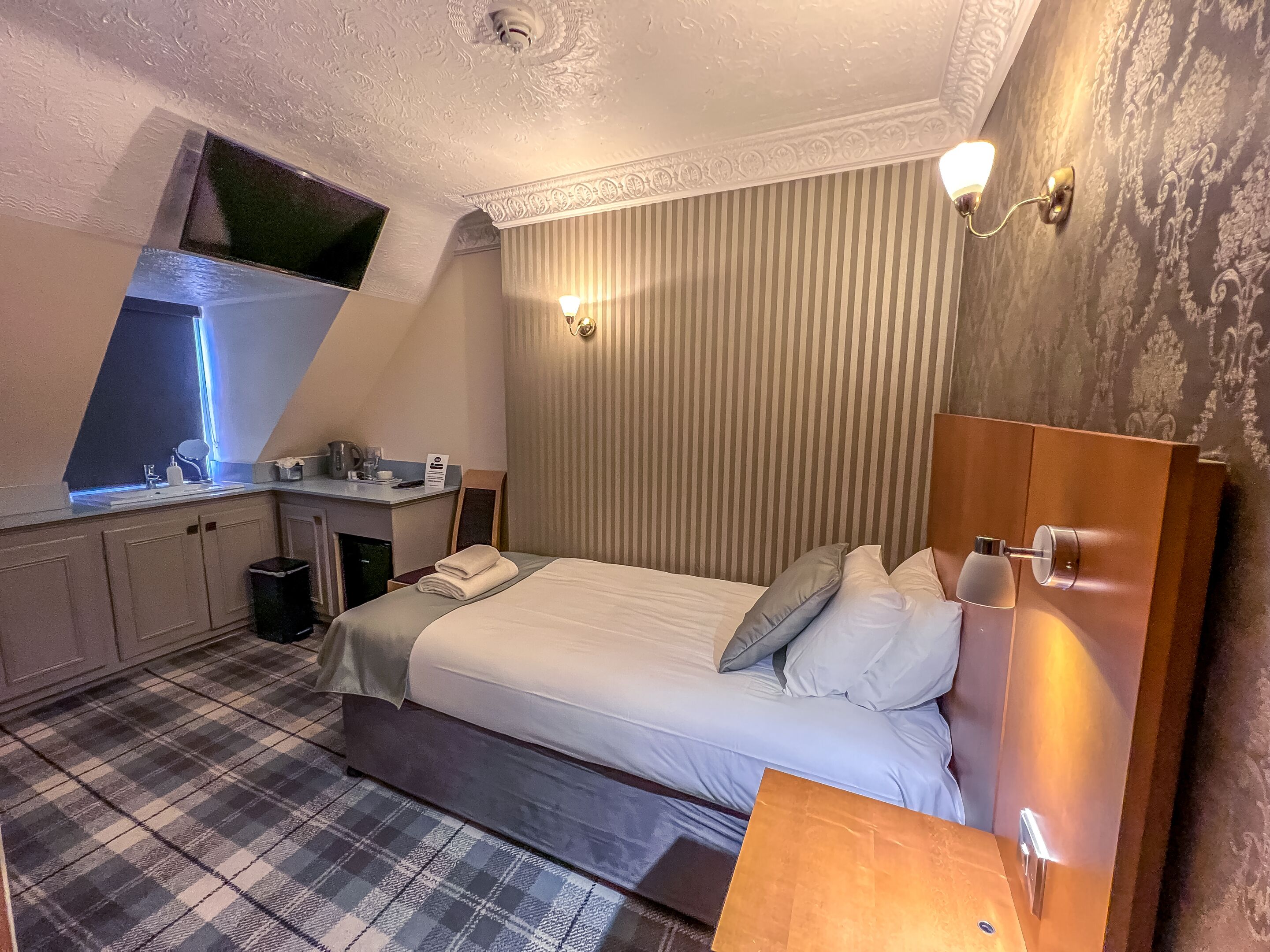 Une chambre à coucher comprenant un lit, une table de chevet, une fenêtre, un bureau avec une chaise et une poubelle.
