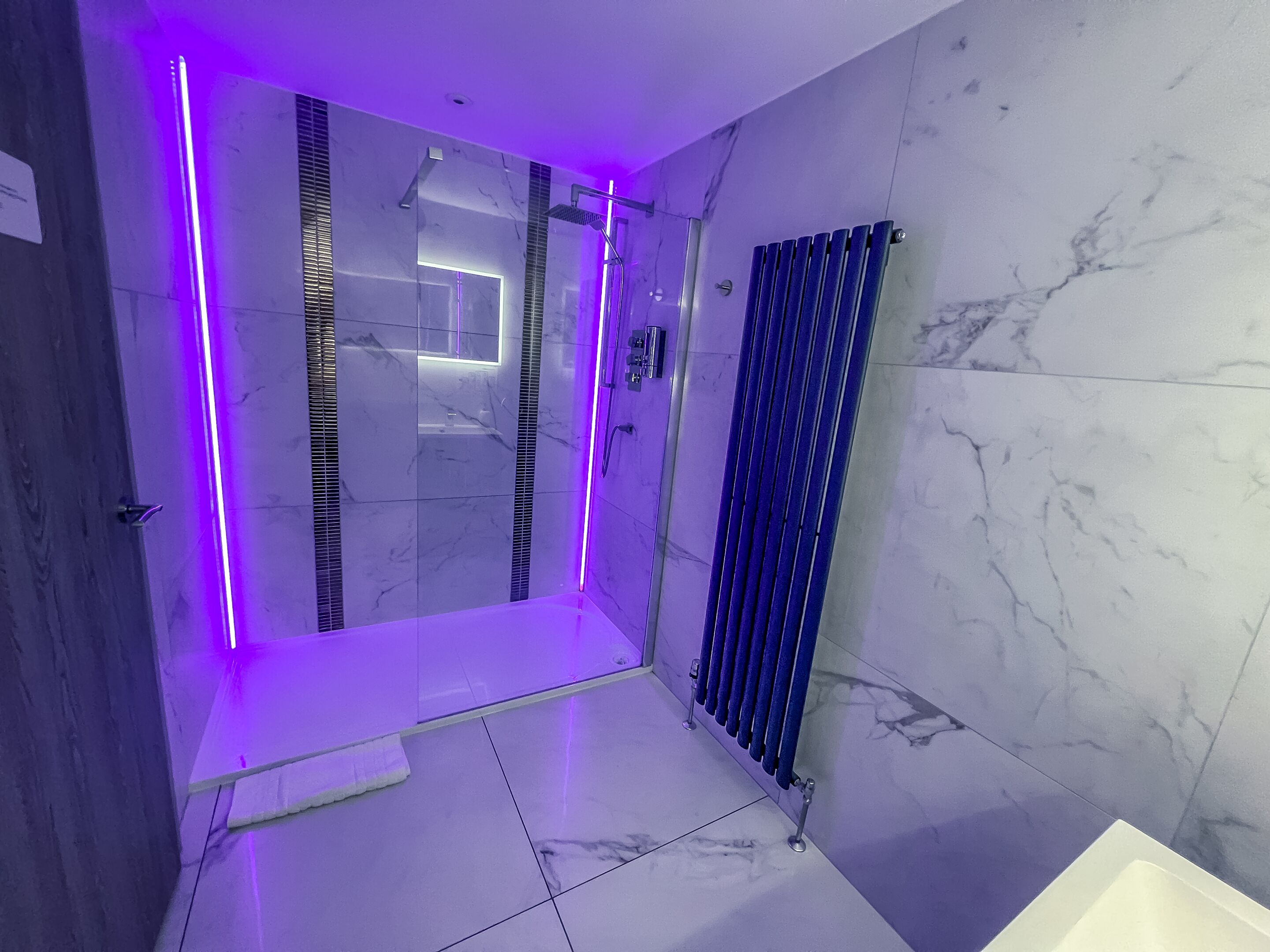 Un baño moderno con mampara de vidrio, radiador azul y paredes de mármol.