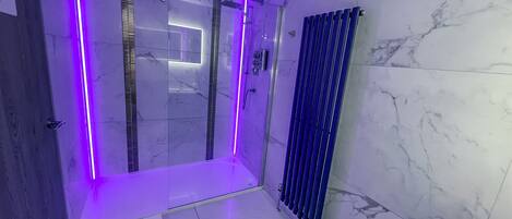 Un baño moderno con mampara de vidrio, radiador azul y paredes de mármol.