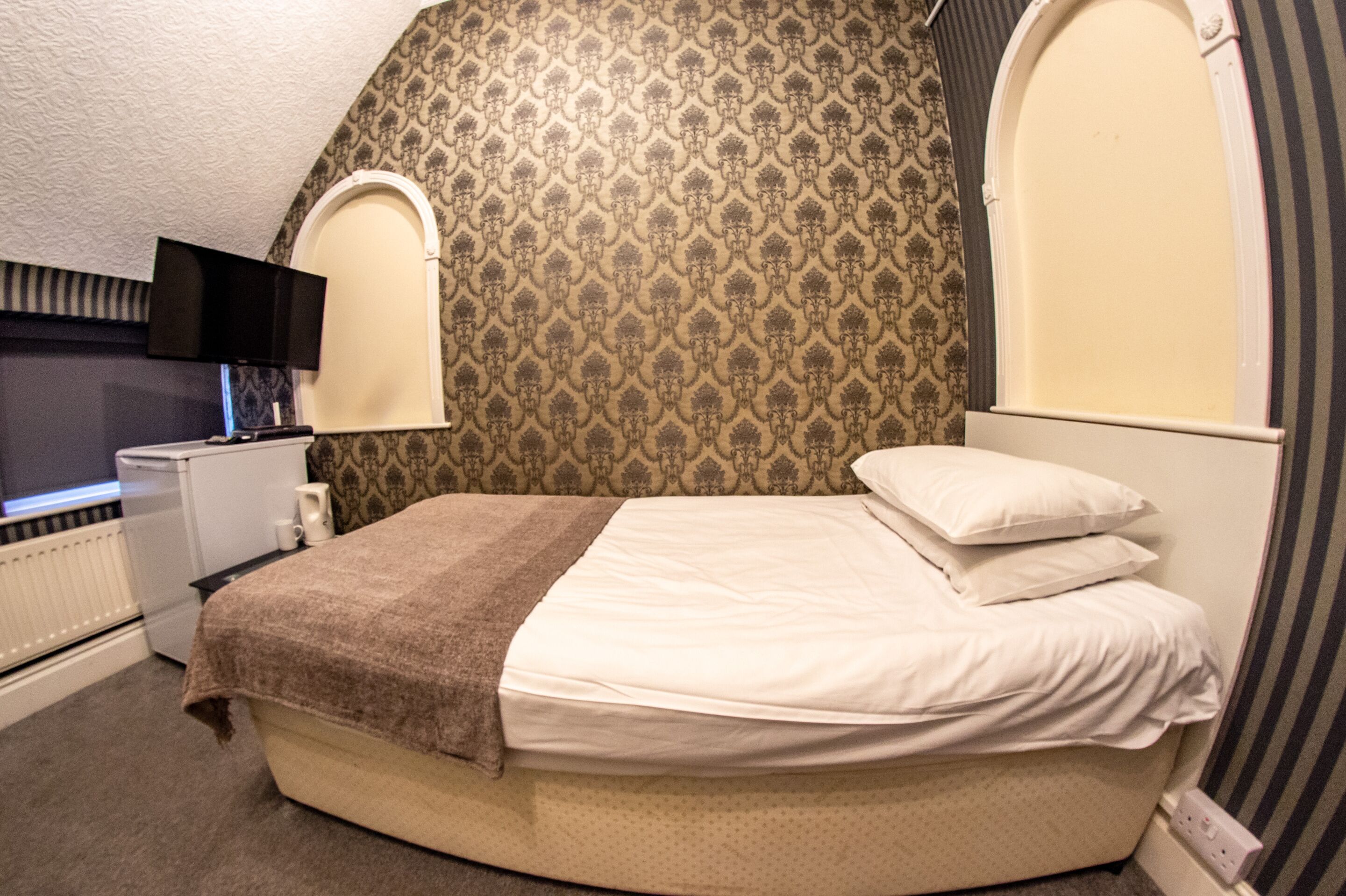 Un dormitorio con una cama, una mesita de noche, una lámpara, un televisor y un radiador.