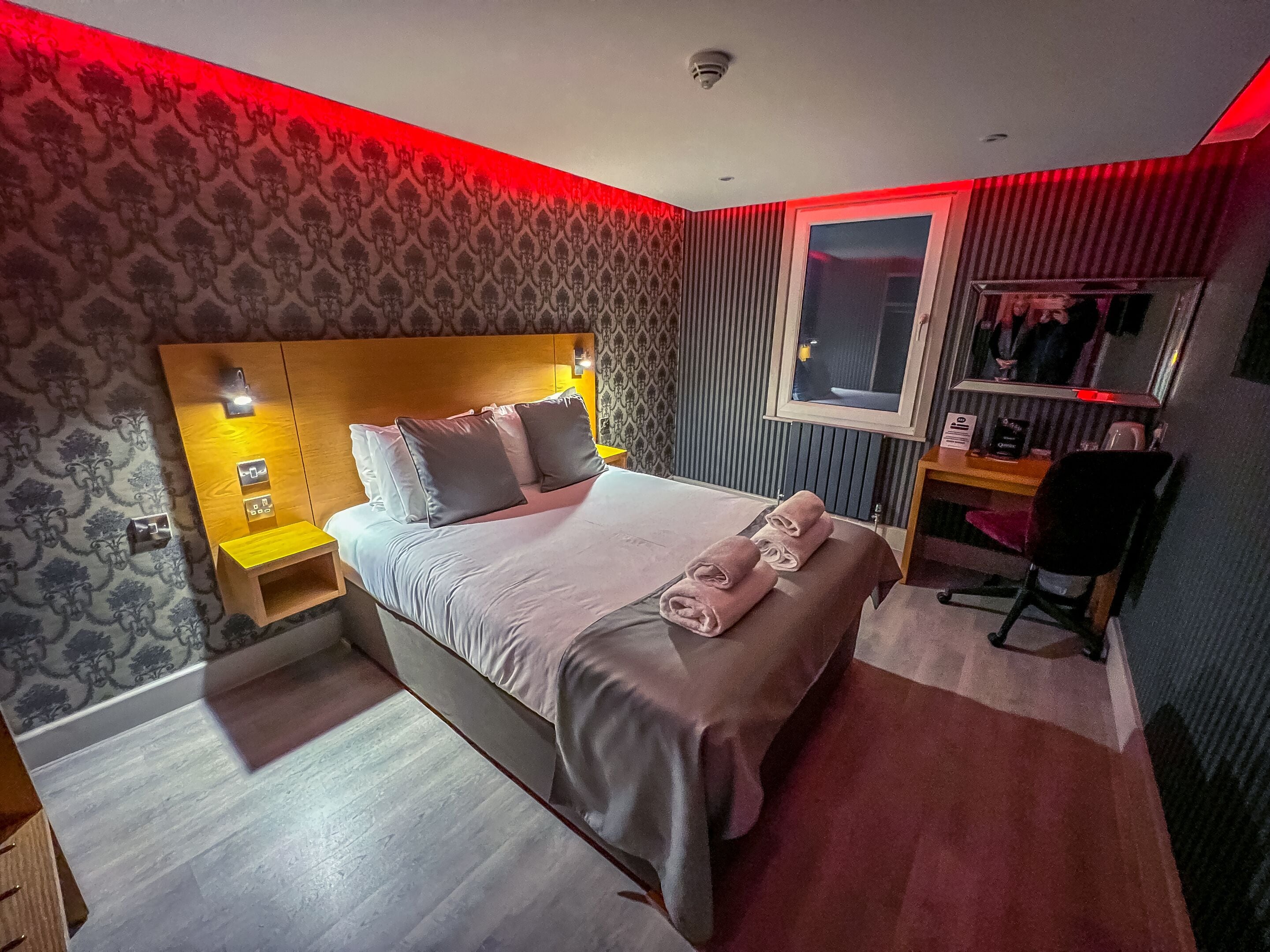 Una habitación de hotel moderna con una cama grande, mesitas de noche, un escritorio y un espejo.