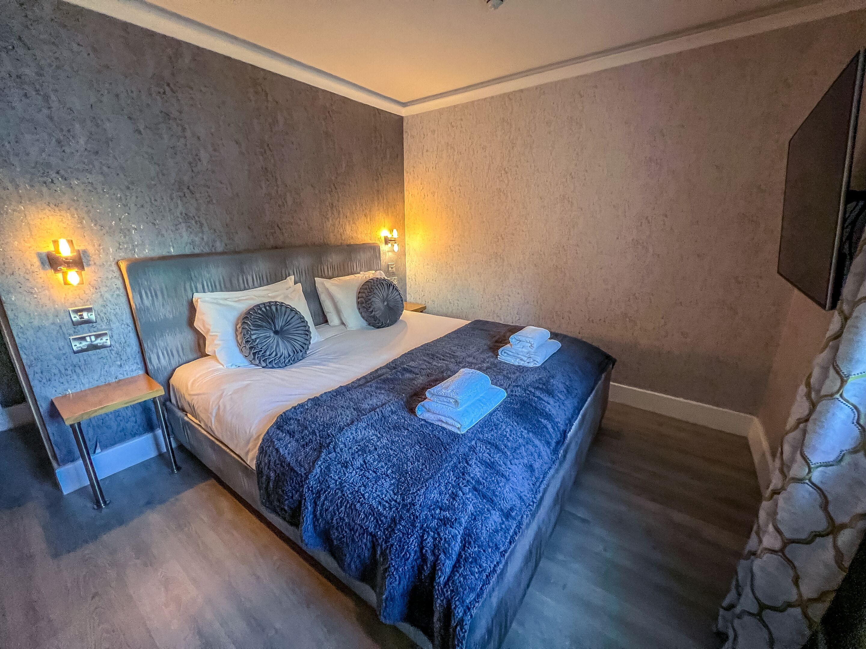 A bedroom with a large bed, two bedside tables, a nightstand, and wall-mounted lights.