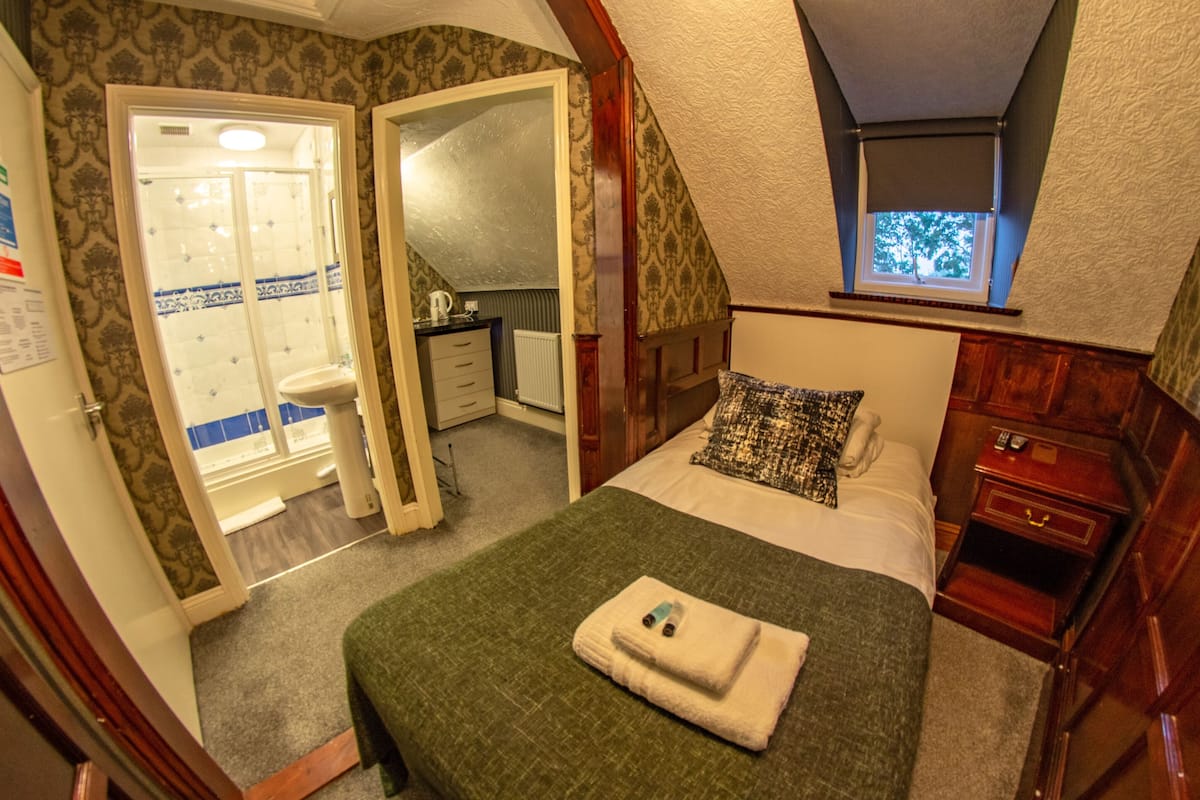 A bedroom with a bed, a window, a bathroom, and a small desk.
