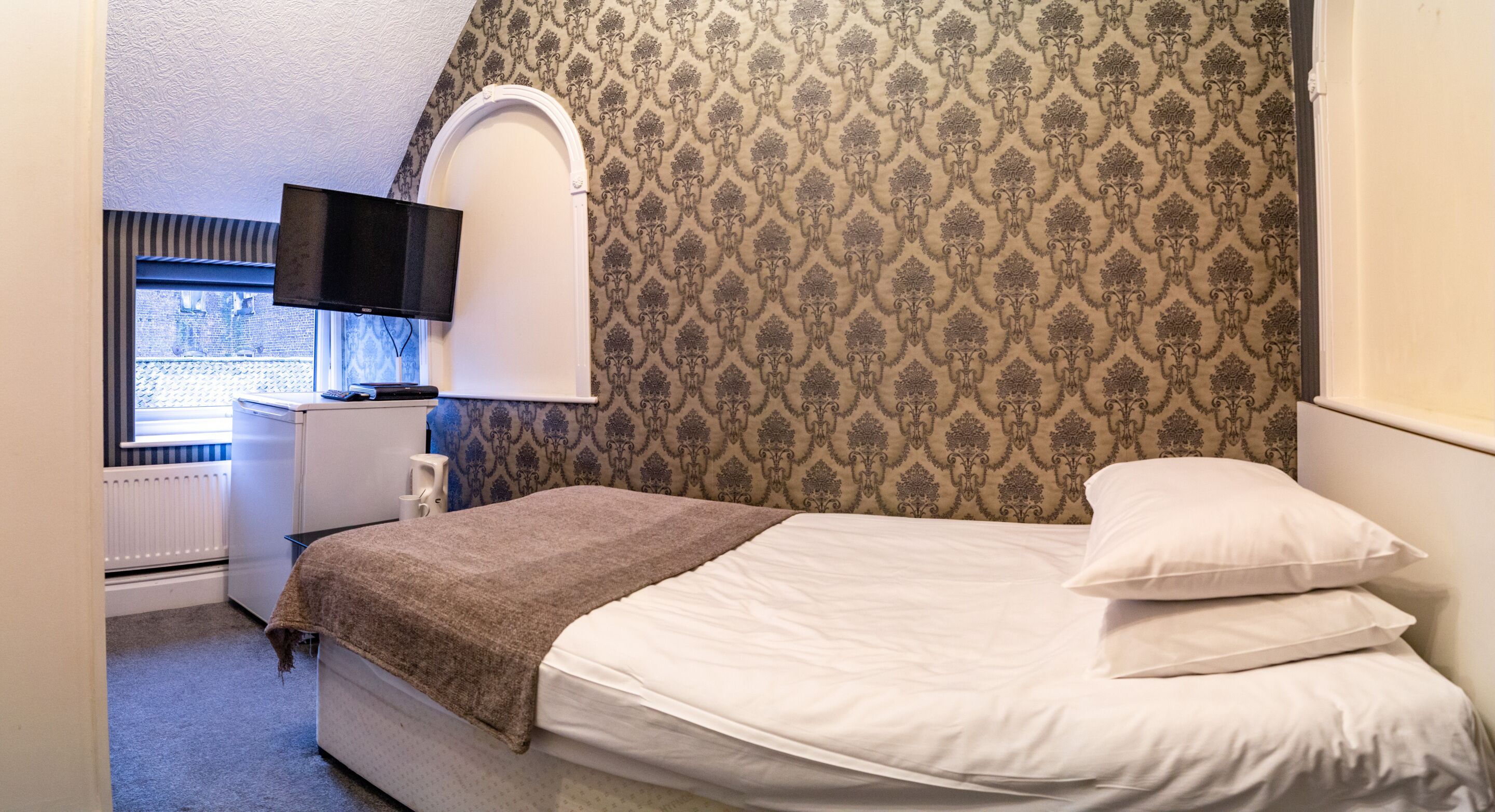 A bedroom with a bed, a TV, a radiator, and a window.