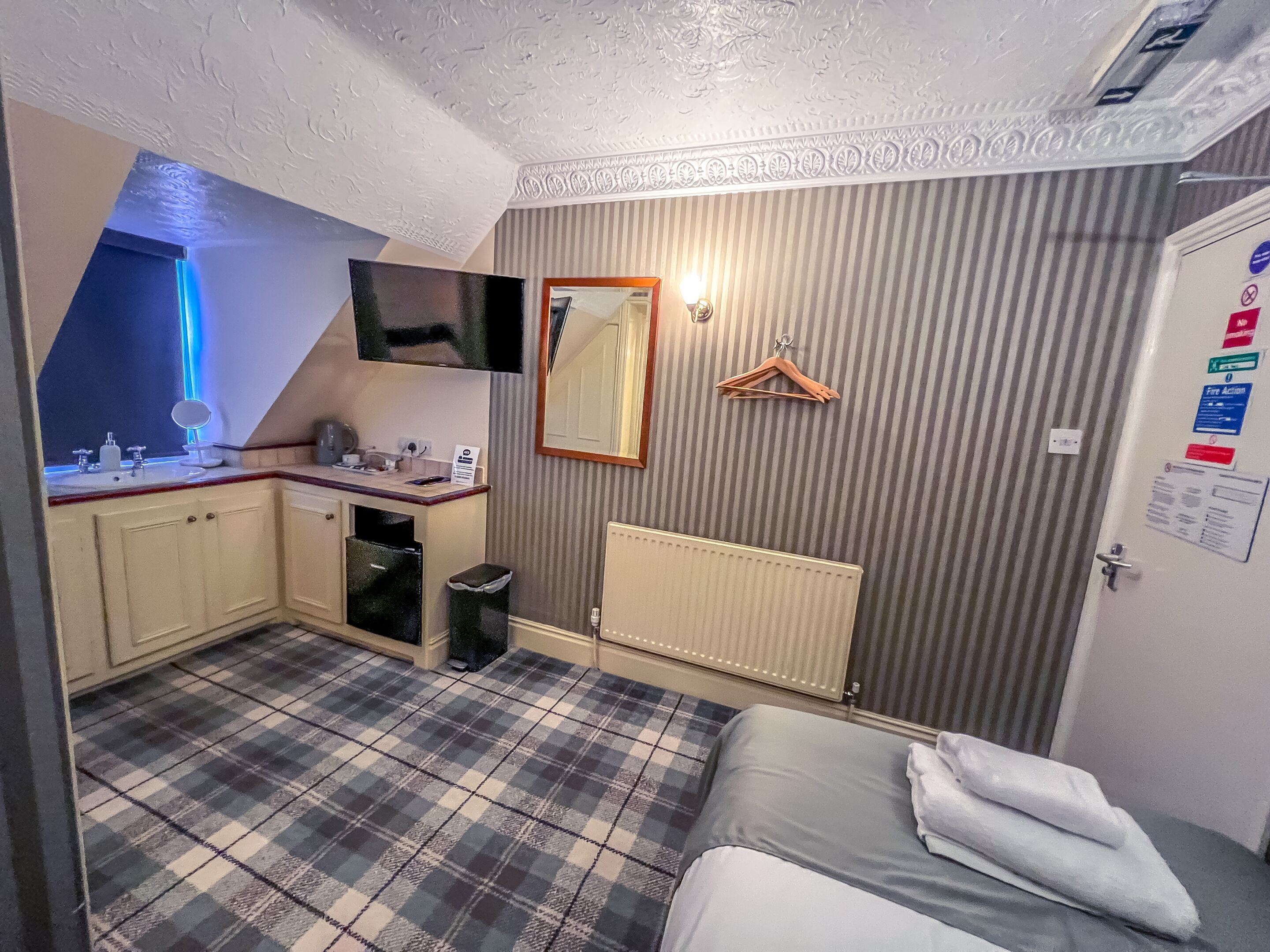 Une petite pièce comprenant un coin cuisine, un lit, un miroir, une télévision et un radiateur.