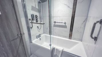 A modern bathroom with a glass-enclosed shower, a white bathtub, and a handrail.