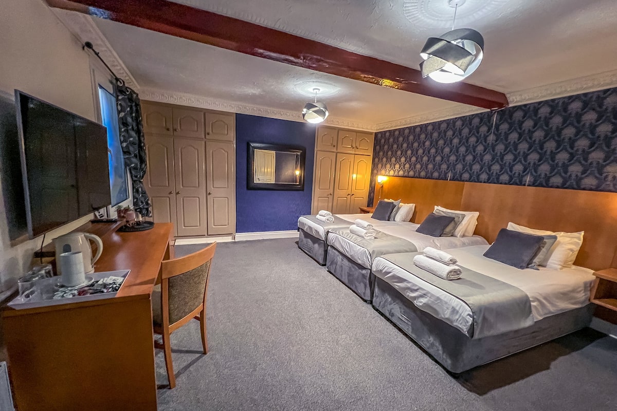 A hotel room with a desk, two beds, a TV, and a mirror.