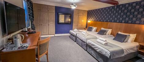 A hotel room with a desk, two beds, a TV, and a mirror.
