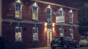 A brick building with a sign for Quayside Hotel, featuring multiple windows and a car parked in front. - The Quayside Hotel and Bar (Boston)