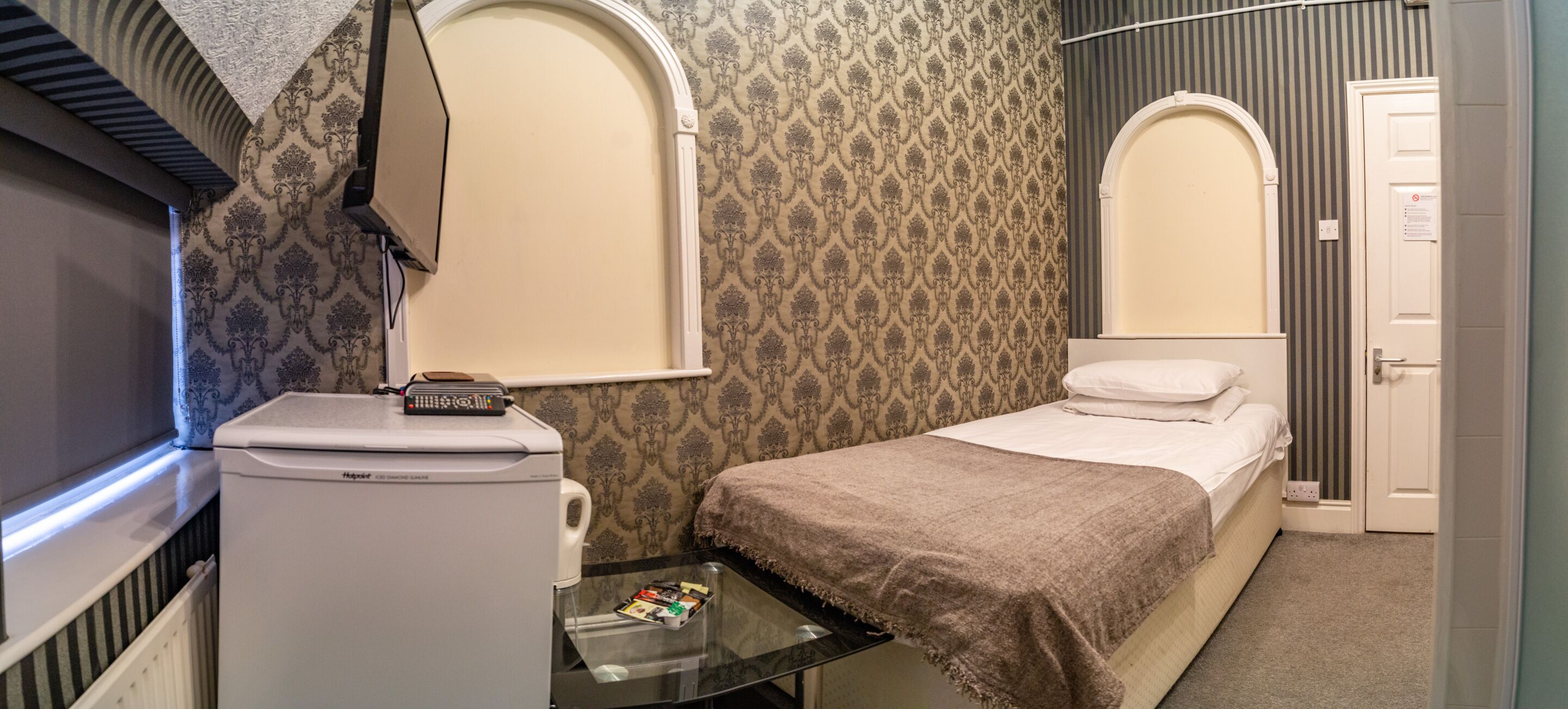 Quarto de hotel com uma cama, uma pequena mesa com um controle remoto, um aquecedor e um espelho sobre a cama.