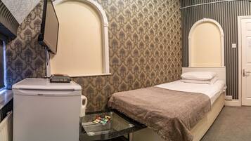 Quarto de hotel com uma cama, uma pequena mesa com um controle remoto, um aquecedor e um espelho sobre a cama.