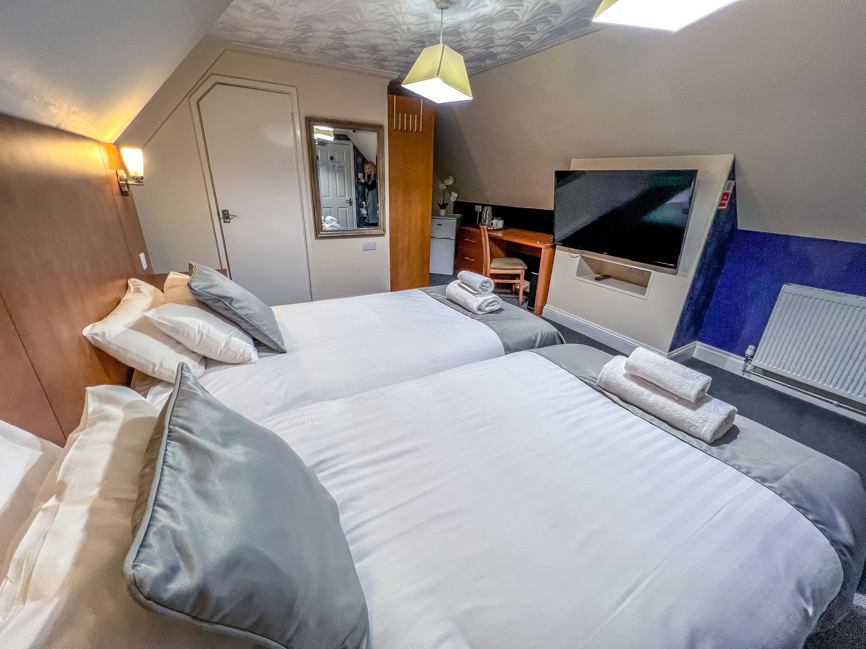 A hotel room with two beds, a desk, a chair, a mirror, and a TV.