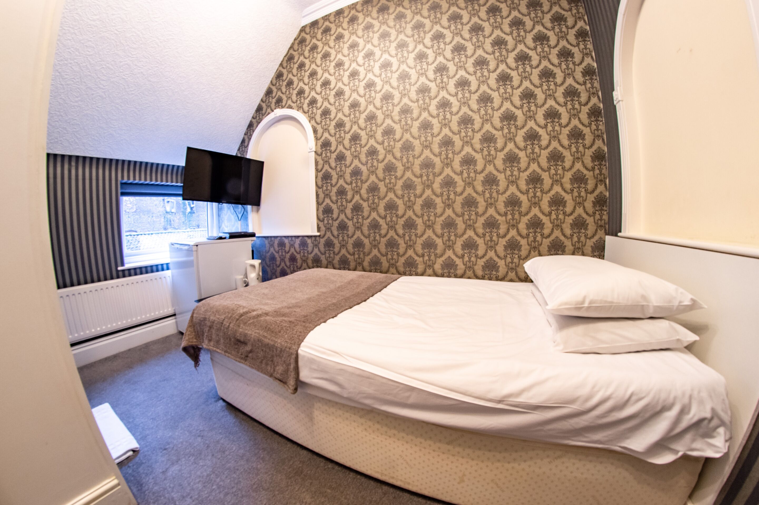 Un dormitorio con cama, televisión, ventana y radiador.