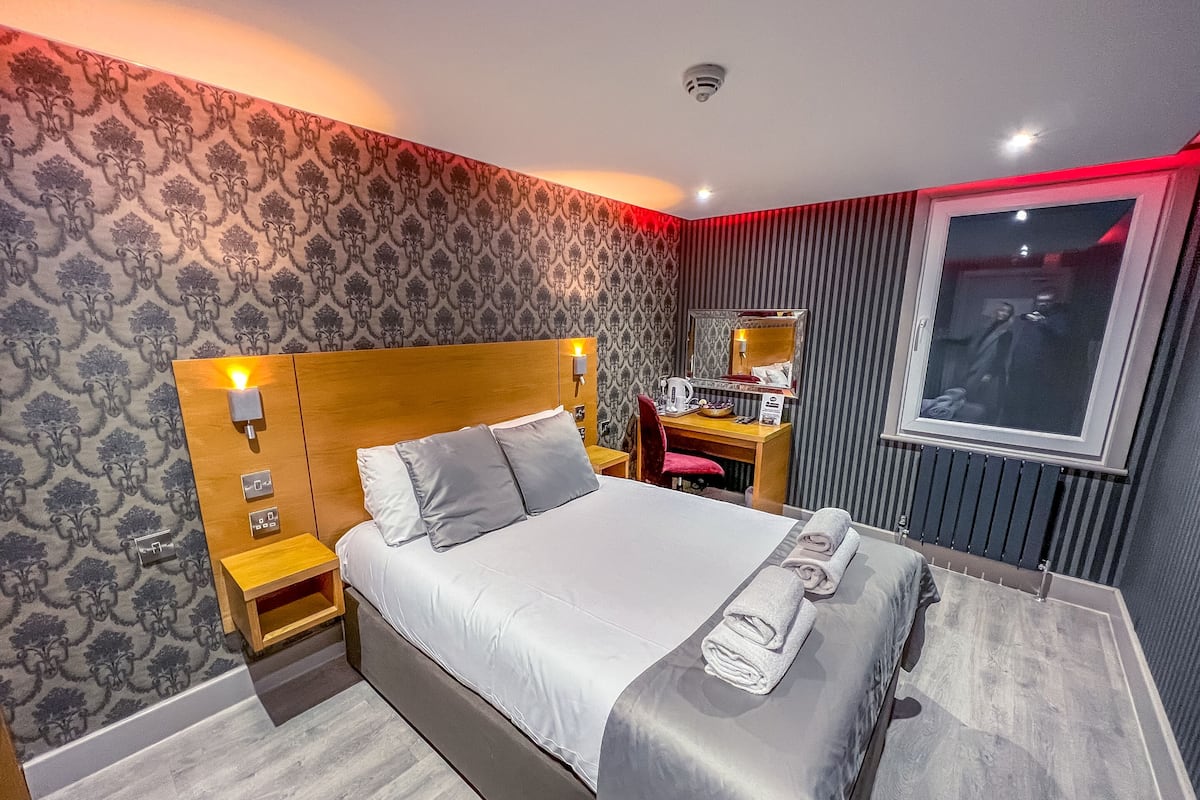 A modern hotel room with a large bed, a desk, and a mirror.