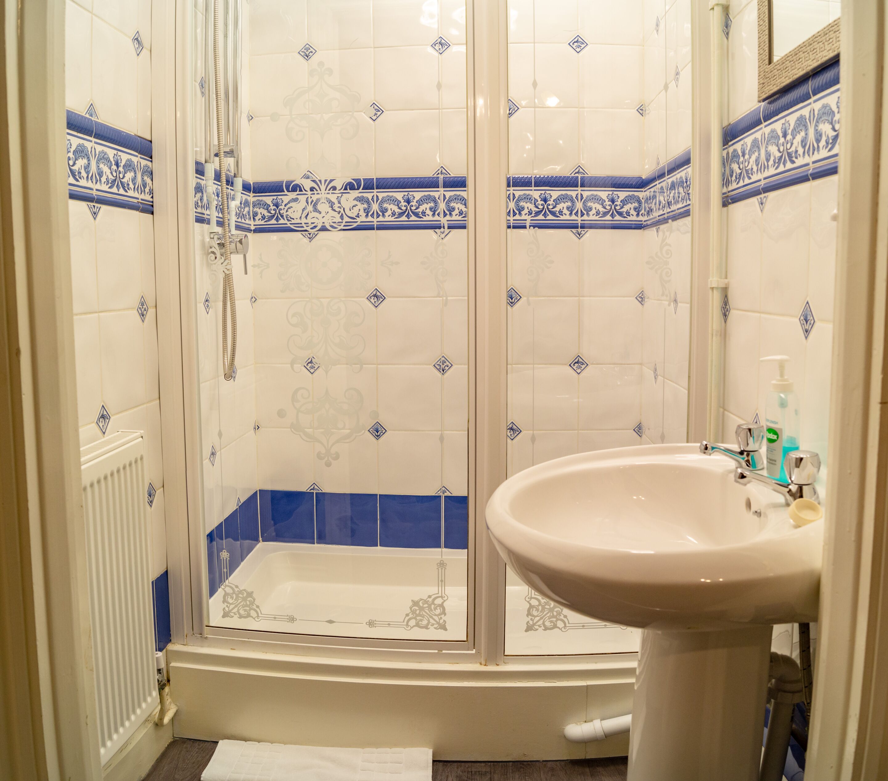 A bathroom with a shower enclosure, a sink, and decorative tiles.